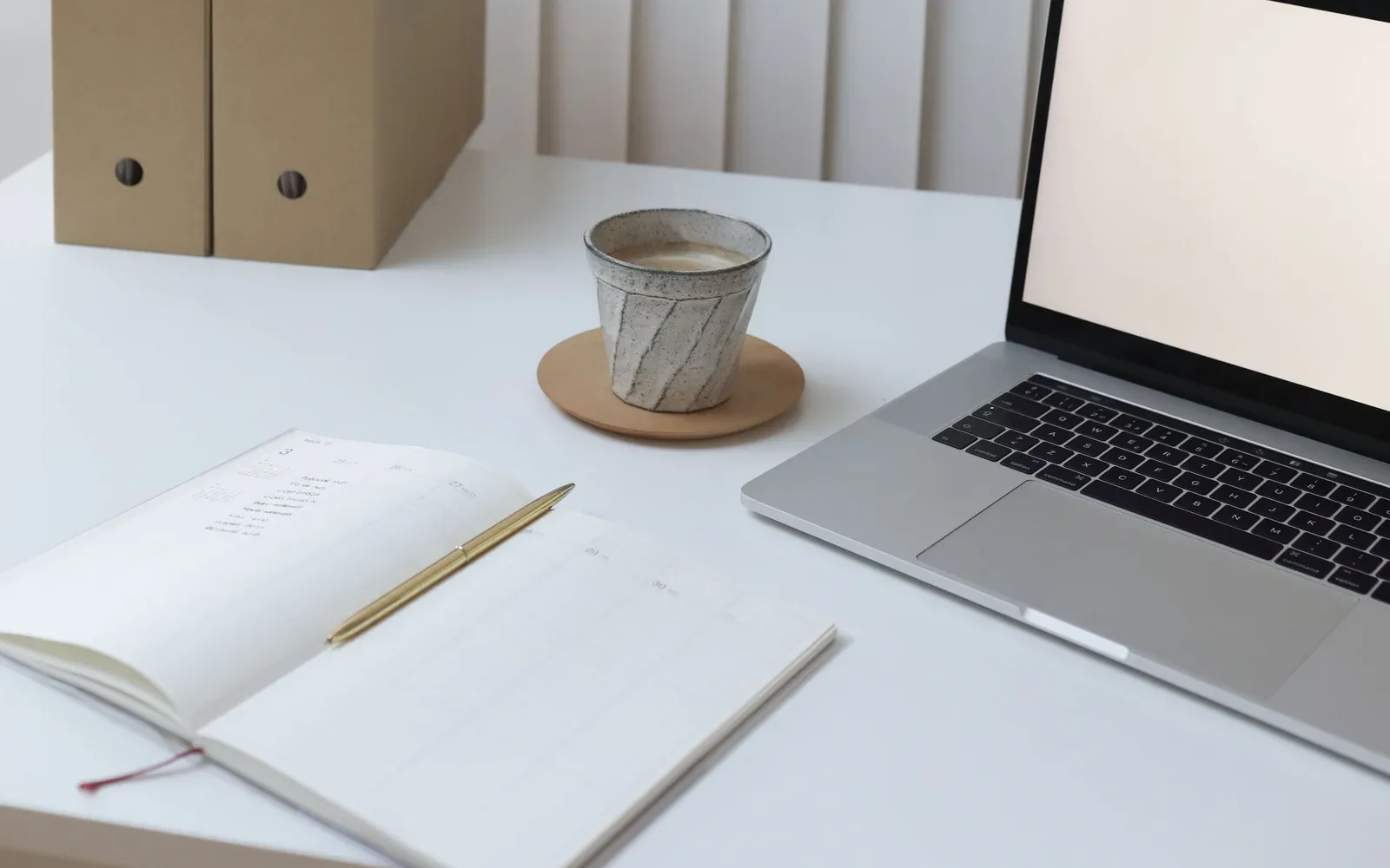 A light workspace with a laptop, notebook and document folders.