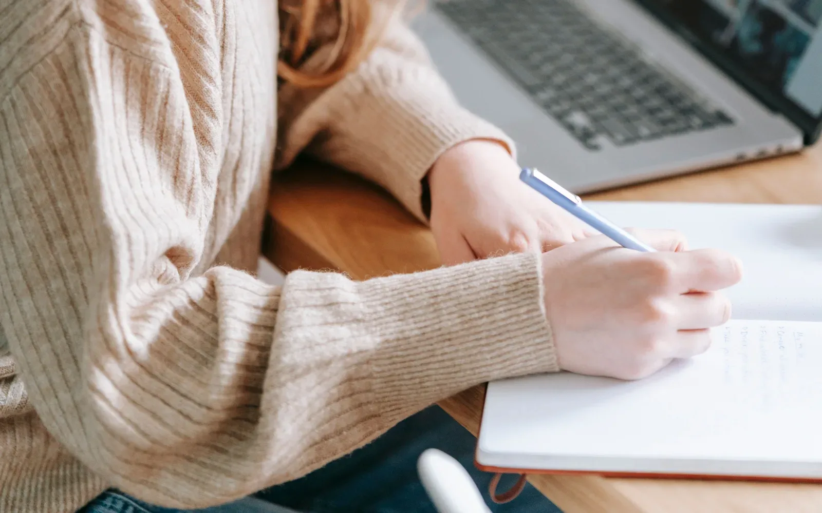 Hands taking handwritten notes next to a laptop.