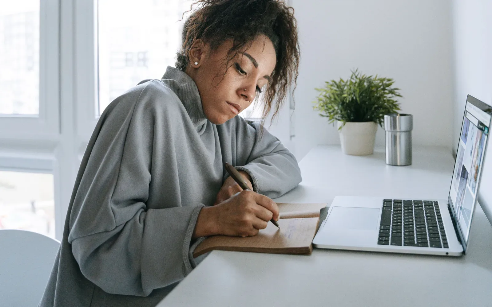 A woman writing notes in a planner beside her laptop.